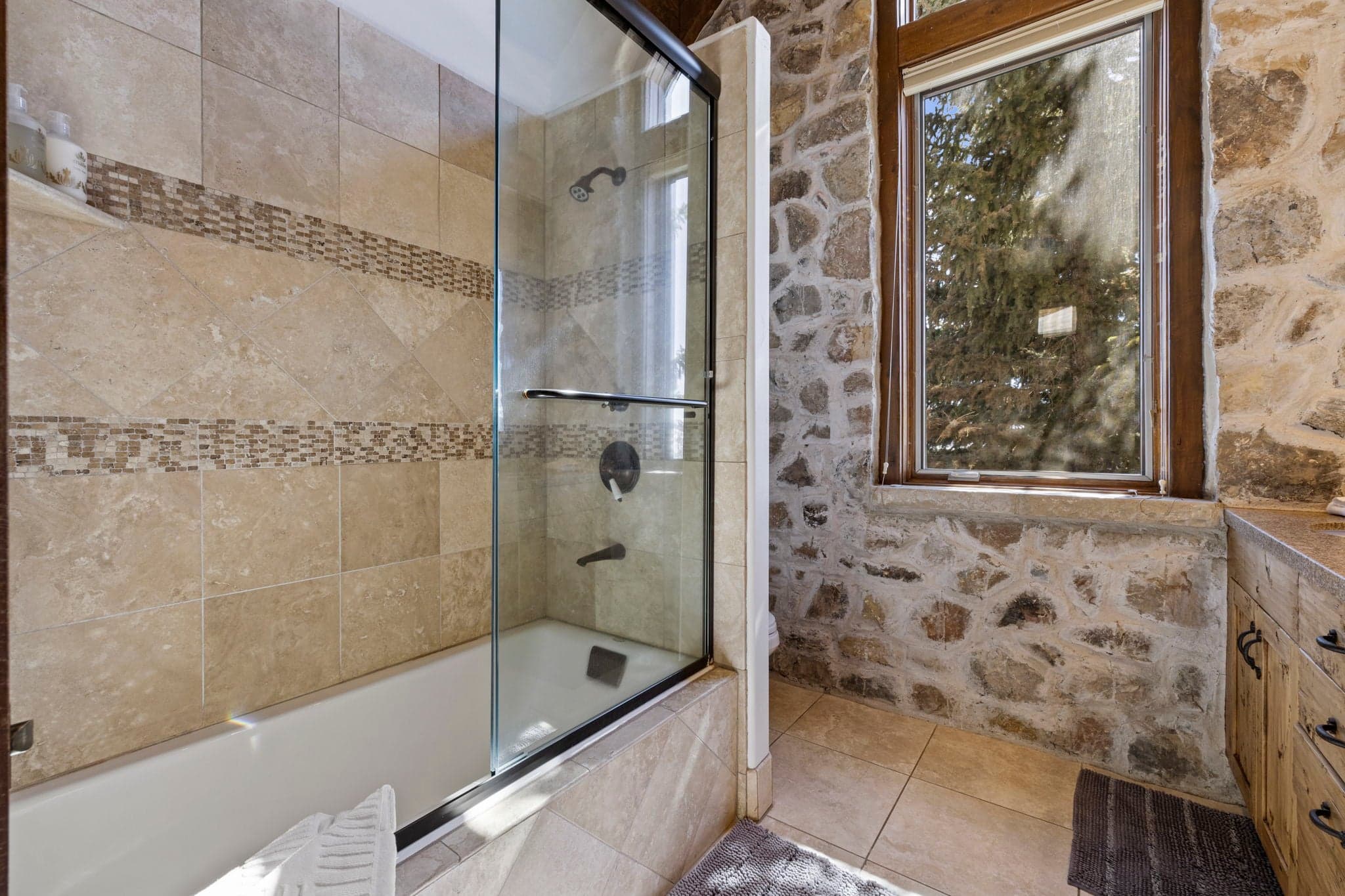 Bathroom with glass-enclosed shower, stone walls, and window with natural light.